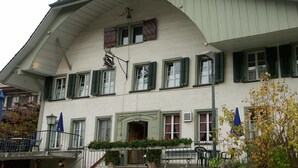 A building with a steeply pitched roof, multiple windows with shutters, and a balcony with plants.