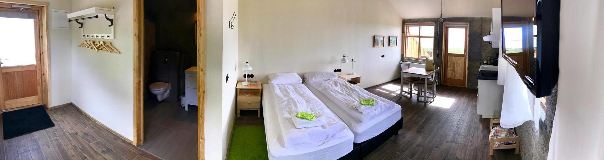 Ein Zimmer mit zwei Betten, einem kleinen Schreibtisch, einem Fenster und Blick ins Freie.