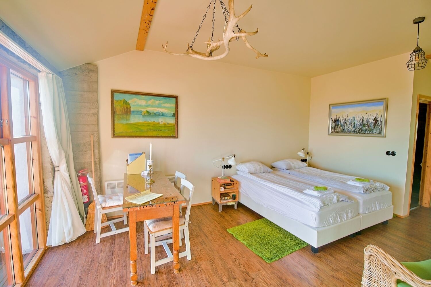 A bedroom with a bed, a desk, and a chair. There is a painting on the wall and a chandelier.