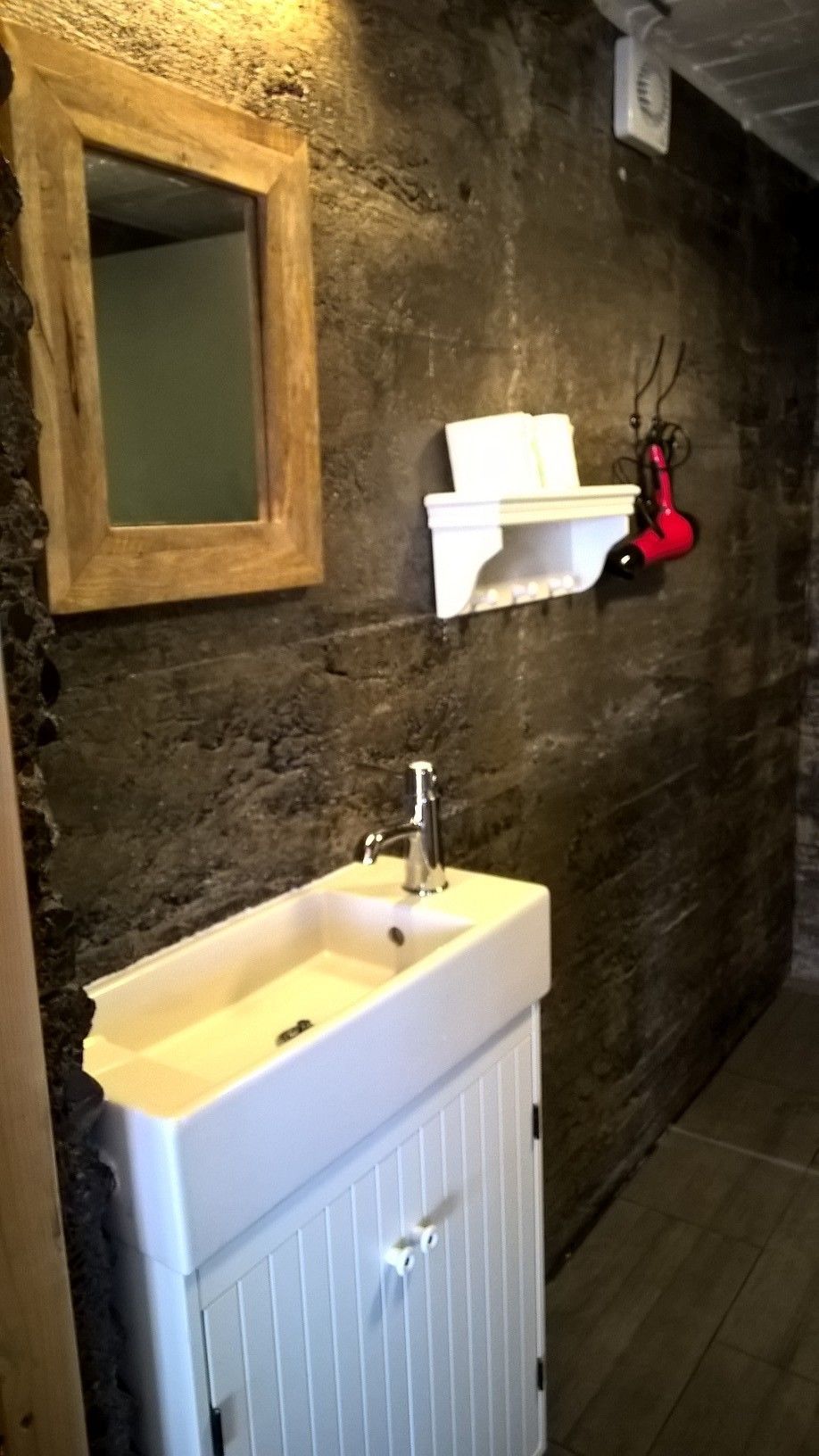 Ein Badezimmer mit einem weißen Waschbecken, einem spiegel mit Holzrahmen und einem roten Fön, der an der Wand befestigt ist.