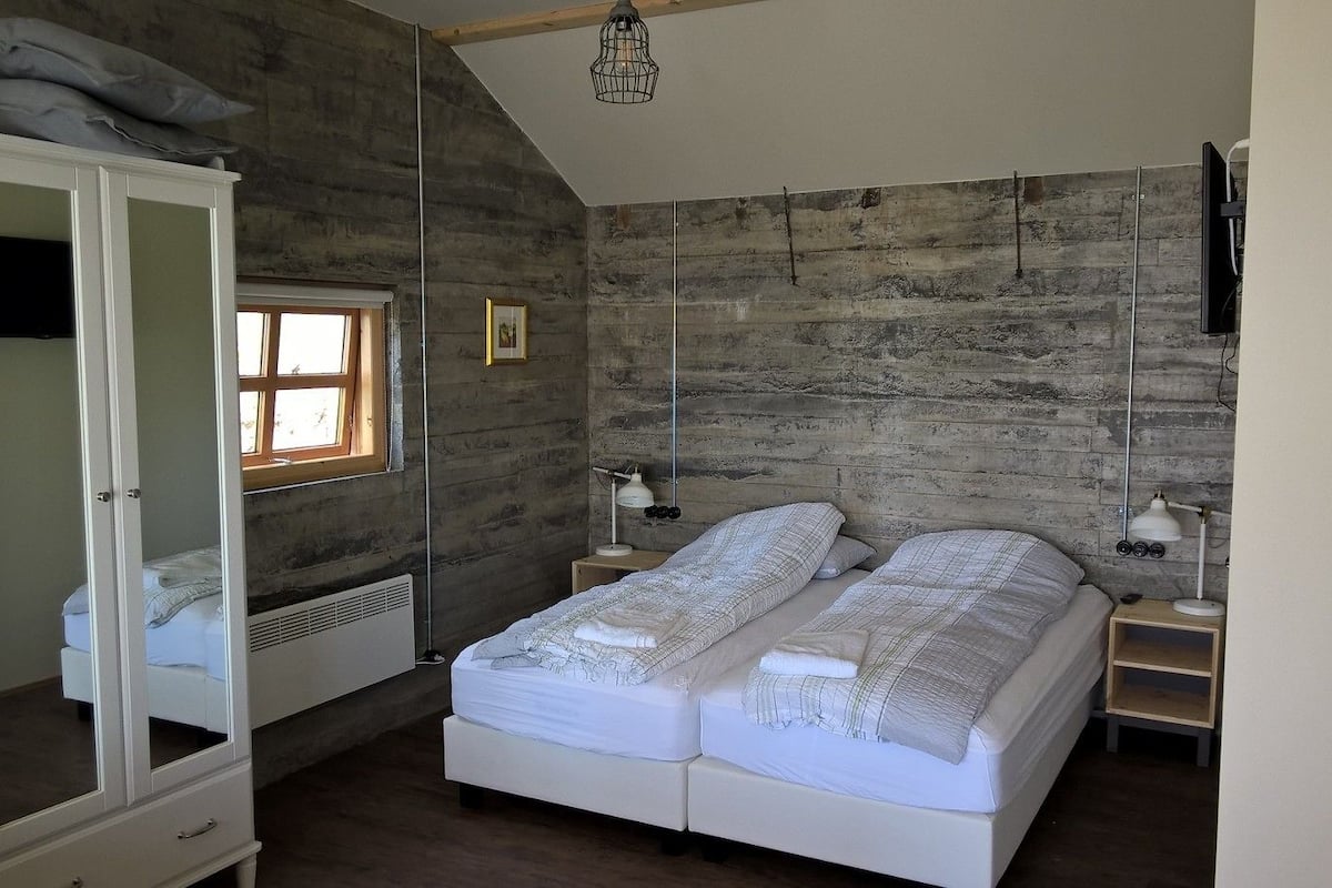 A bedroom with a large bed, a wardrobe, a window, and a wooden wall.