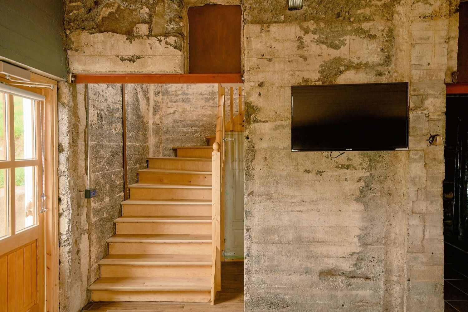 Una escalera de madera en una habitación rústica con una pared de piedra y un televisor de pantalla plana montado en ella.