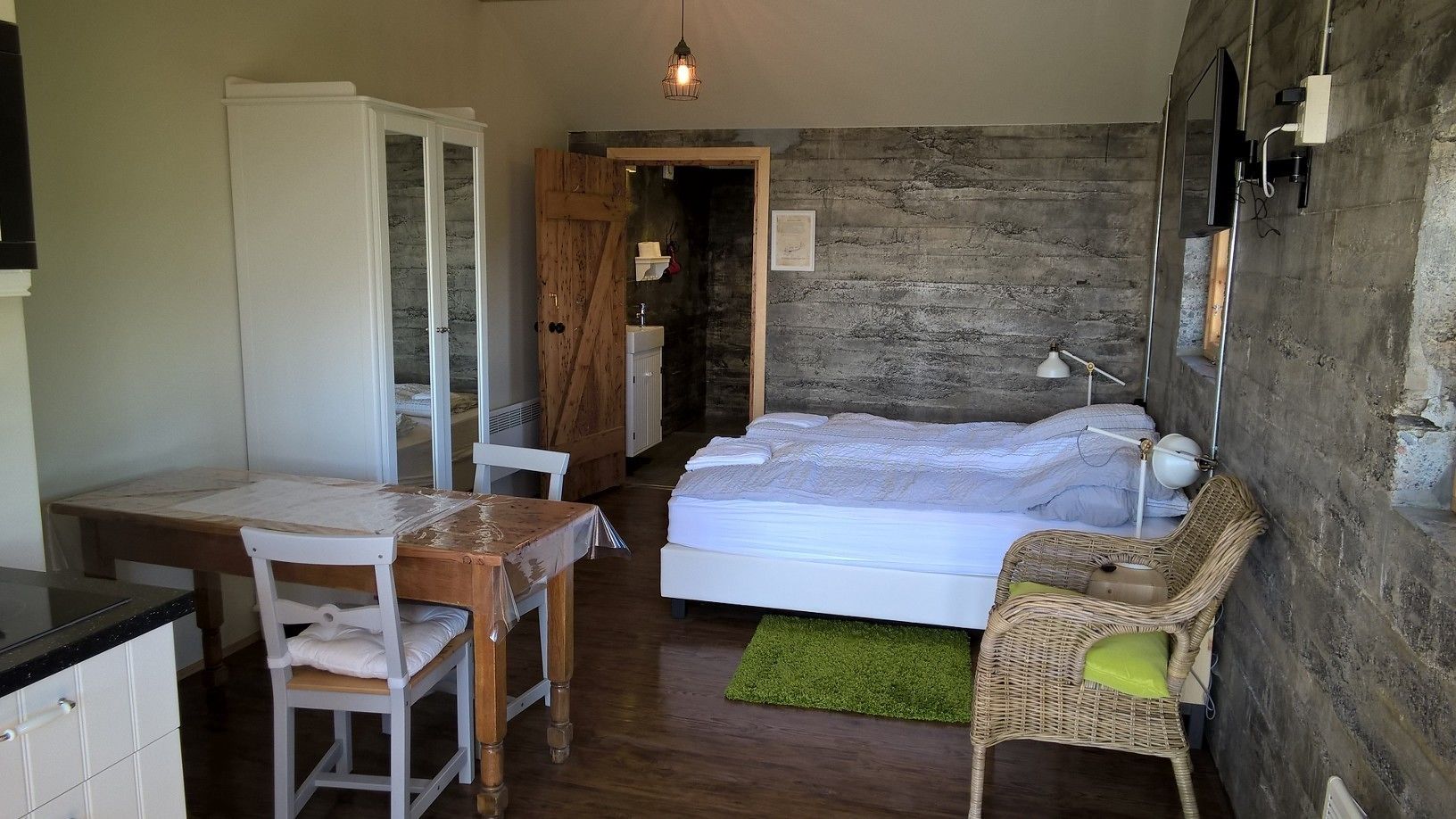A compact bedroom with a bed, a small table, a chair, and a green rug.