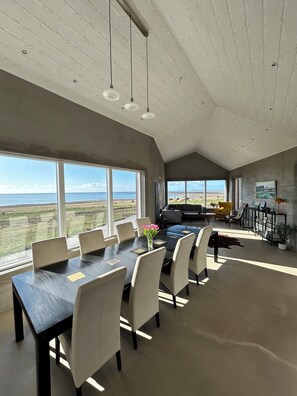 Un comedor amplio con una mesa grande y sillas, ventanas panorámicas que ofrecen vistas al paisaje, y una cocina moderna al fondo.