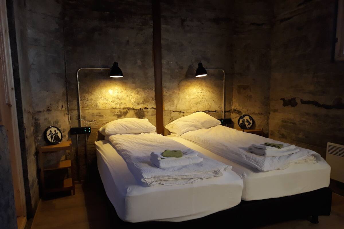 A room with two beds, each with a lamp and a small table beside them.
