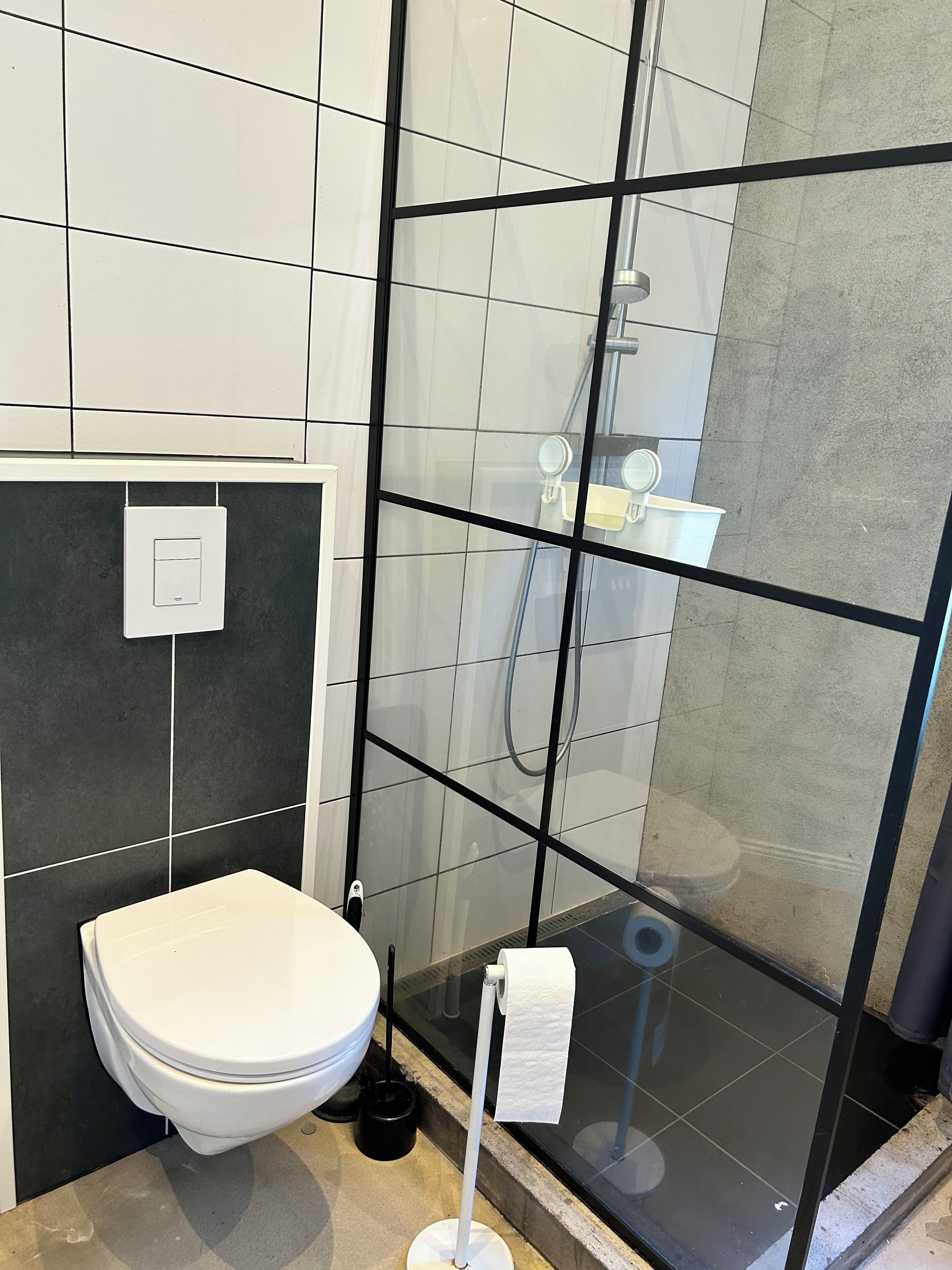 Un baño moderno con inodoro, cabina de ducha de vidrio y un dispensador de papel higiénico a la vista.