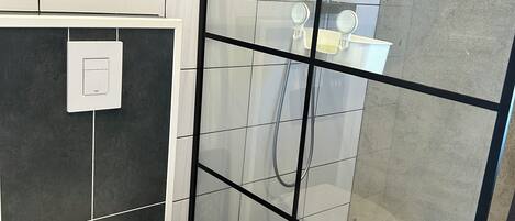 Un baño moderno con inodoro, cabina de ducha de vidrio y un dispensador de papel higiénico a la vista.