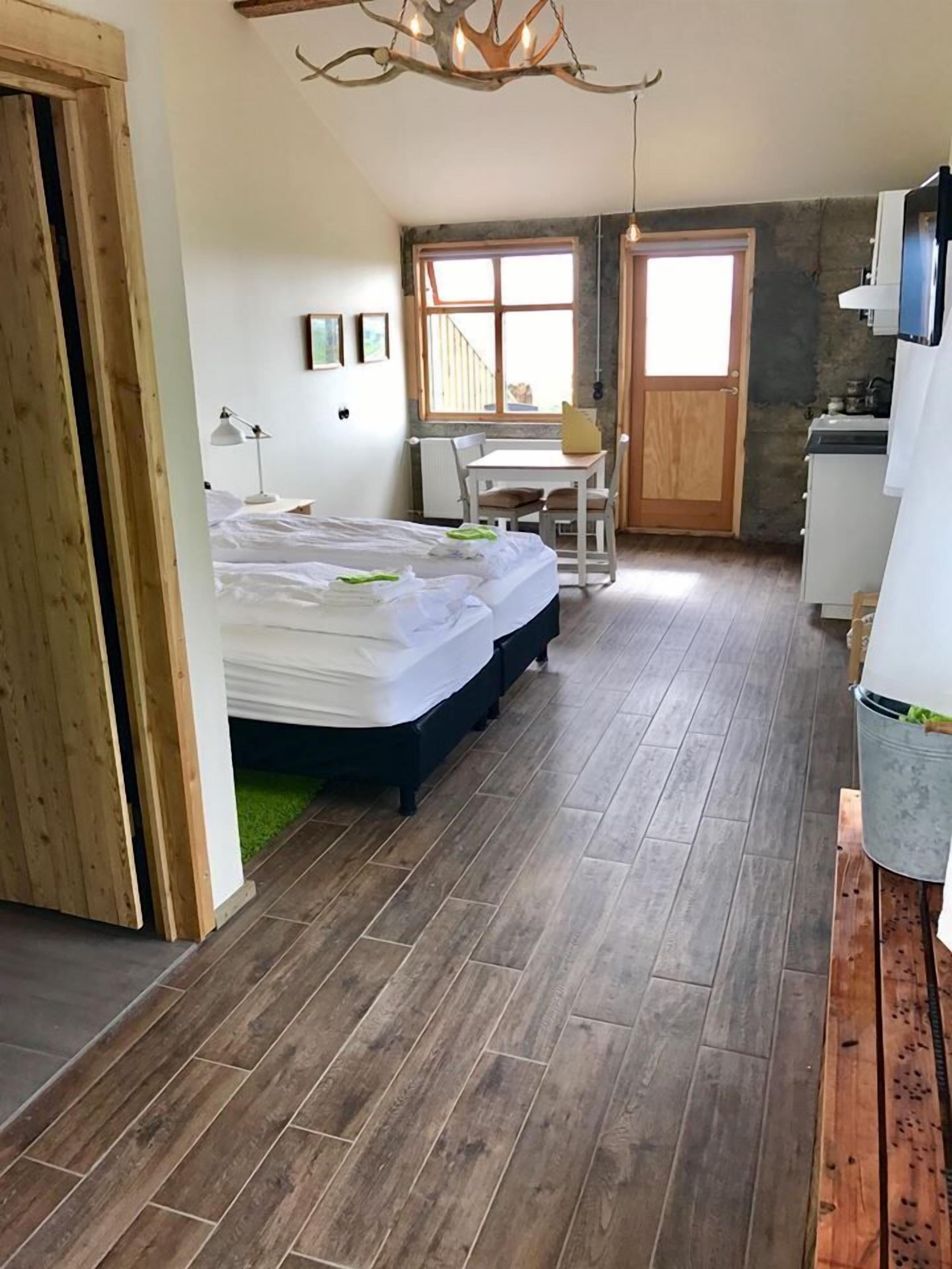 A room with a bed, a desk, a chair, a window, and a kitchenette.