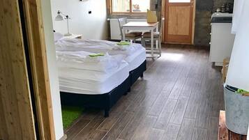 A room with a bed, a desk, a chair, a window, and a kitchenette.