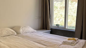 A bedroom with two beds, a window with curtains, and a view of a mountainous landscape.