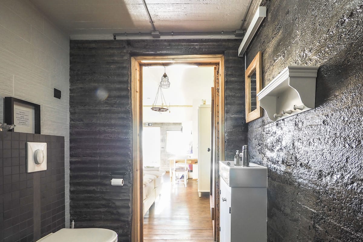 A narrow bathroom with a toilet, sink, and a wooden door leading to a hallway.