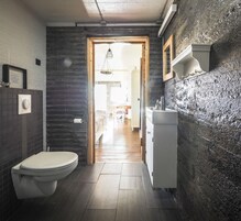 Un baño estrecho con inodoro, lavamanos y una puerta de madera que da a un pasillo.