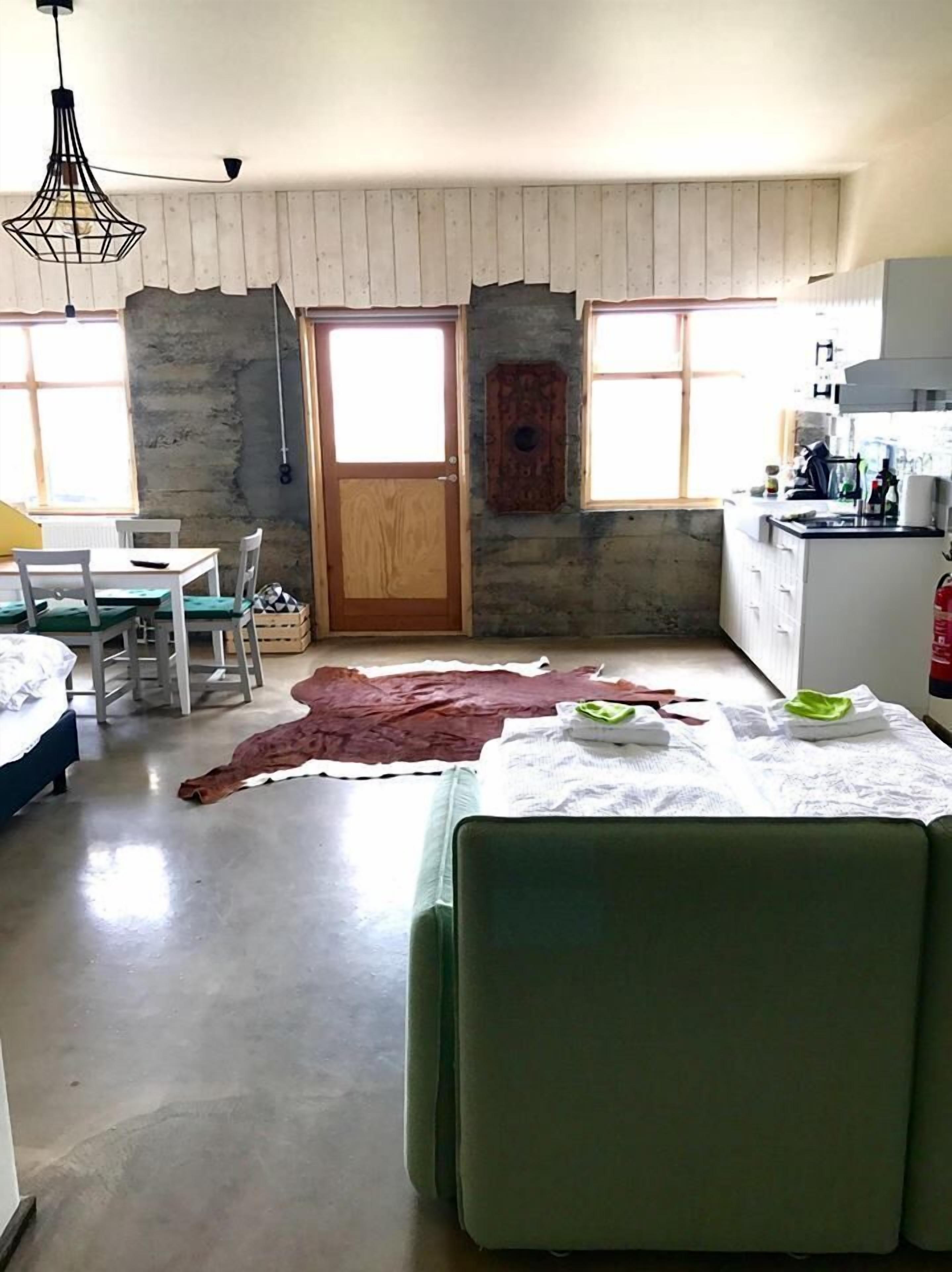 Une pièce comprenant une table à manger, des chaises, un canapé vert, une porte en bois et un coin cuisine avec un évier et des placards.