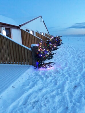 A snow-covered yard with a wooden fence and a house. - The Garage (Rangárþing eystra)