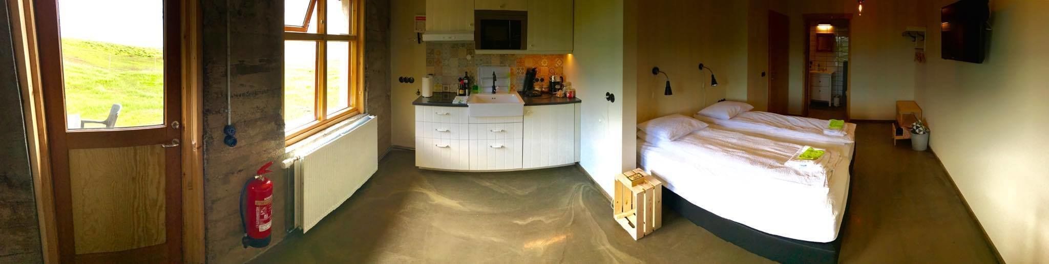 A compact room with a bed, a small kitchenette, a window with a view, and a fire extinguisher.