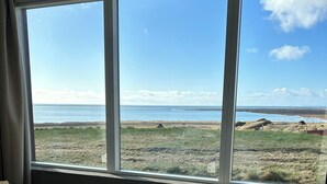 A hotel room with a large window offering a view of a beach and the sea. - The Garage (Rangárþing eystra)