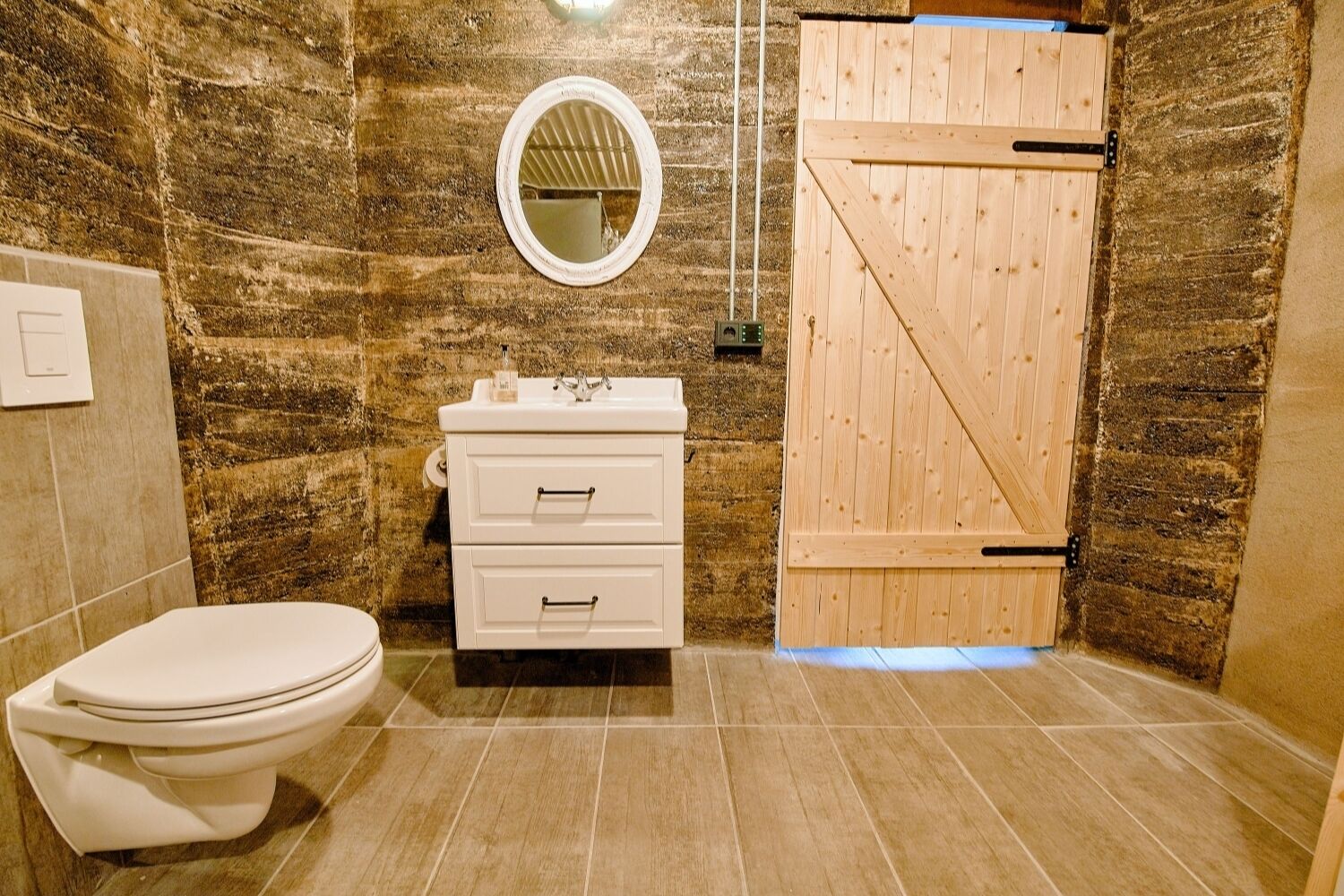 A bathroom with a toilet, a sink with a mirror, and a wooden door.