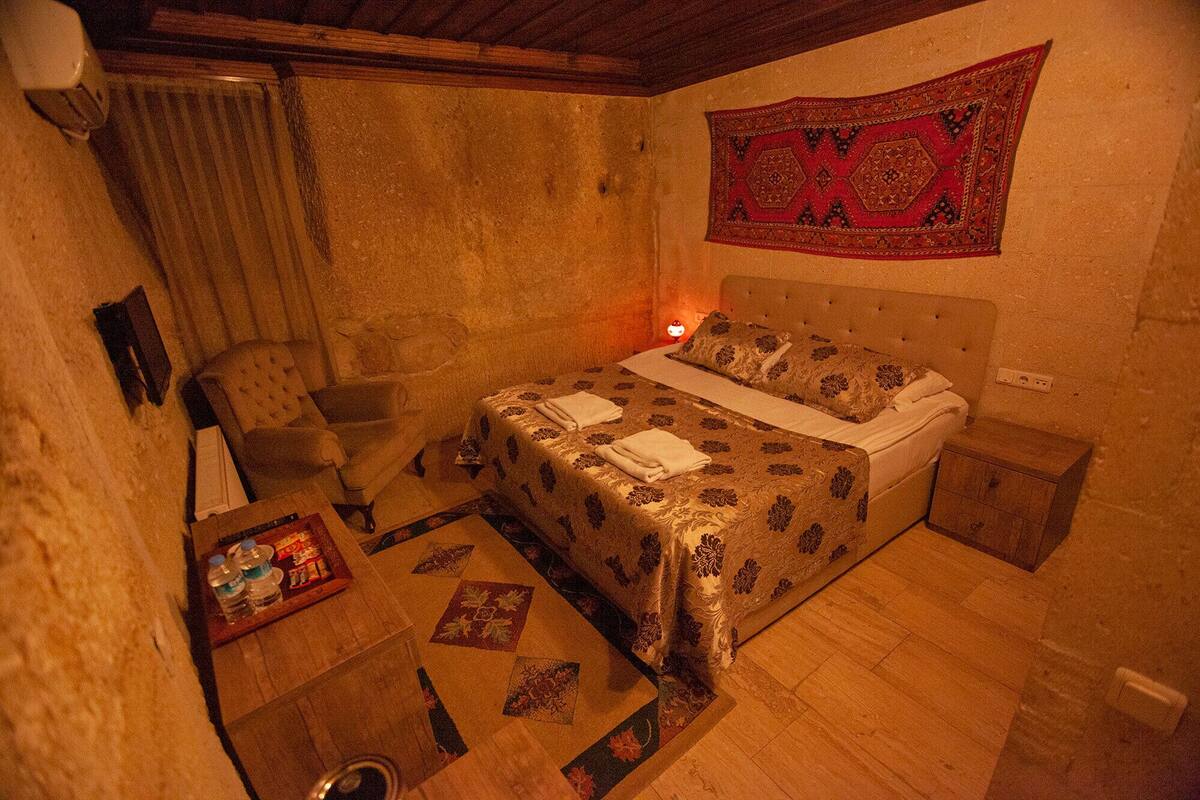 A bedroom with a bed, a nightstand, a chair, a table with bottles, and a tapestry on the wall.