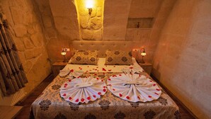 Une pièce chaleureuse avec un mur en pierre, un lit recouvert d’une couvre-lit à motifs et deux lampes de chevet.