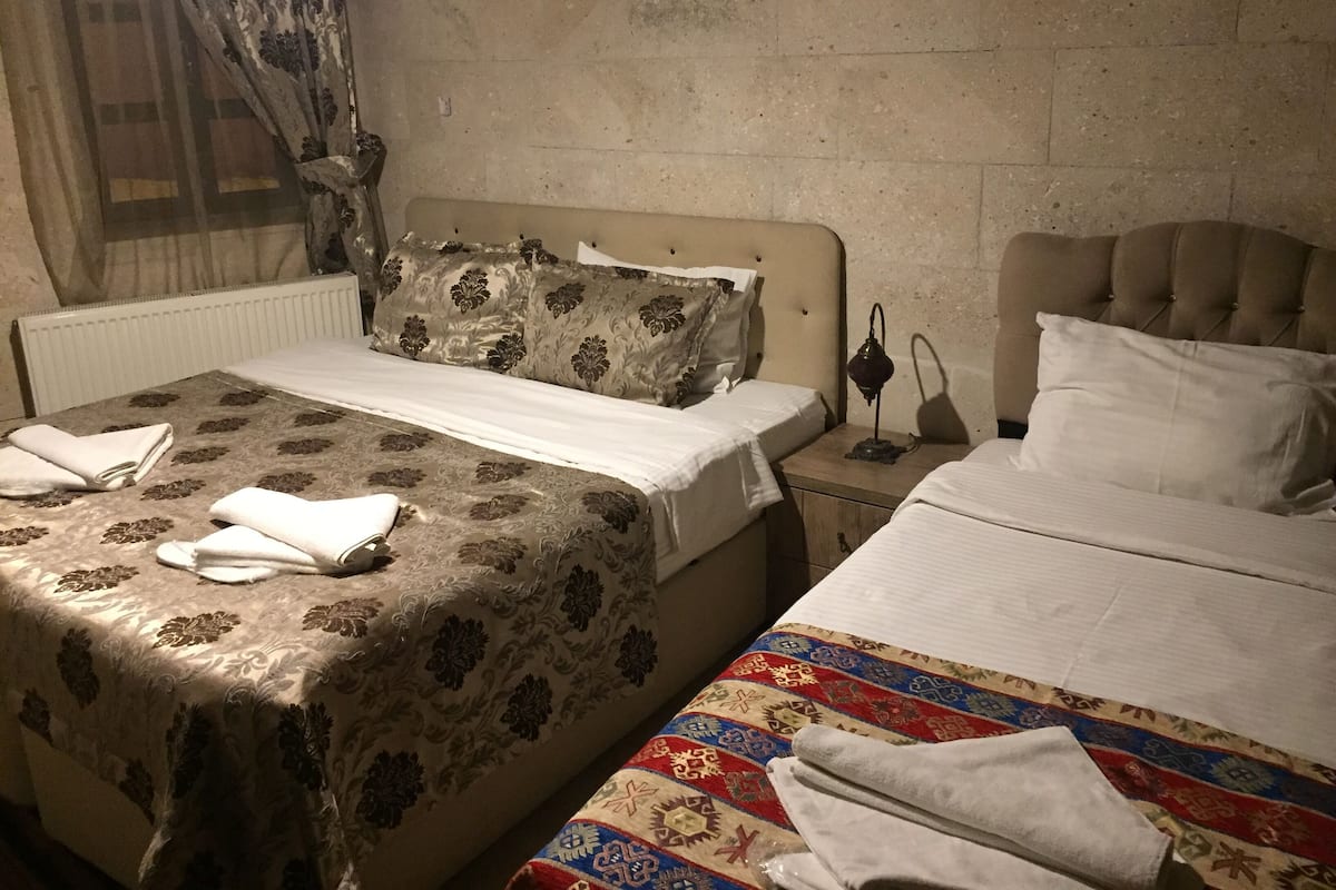 A hotel room with two beds, one with a patterned bedspread and the other with a colorful one. There are towels on the beds and a nightstand with a lamp.