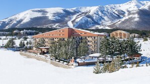 A snow-covered mountain resort with multi-story buildings, a ski lift, and a clear blue sky. - Magnola Palace Hotel (Ovindoli)