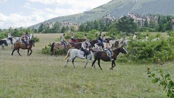 Un groupe de personnes à cheval dans un champ verdoyant, avec des bâtiments en arrière-plan.