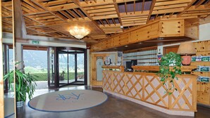 A reception area with a wooden reception desk, a potted plant, and a view of the outdoors. - Magnola Palace Hotel (Ovindoli)