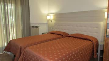 A hotel room with two beds, a headboard, a nightstand, a lamp, and a window with curtains.