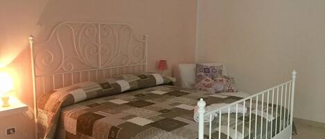 A neatly made bed with a patterned quilt, a white metal headboard, and a bedside lamp.