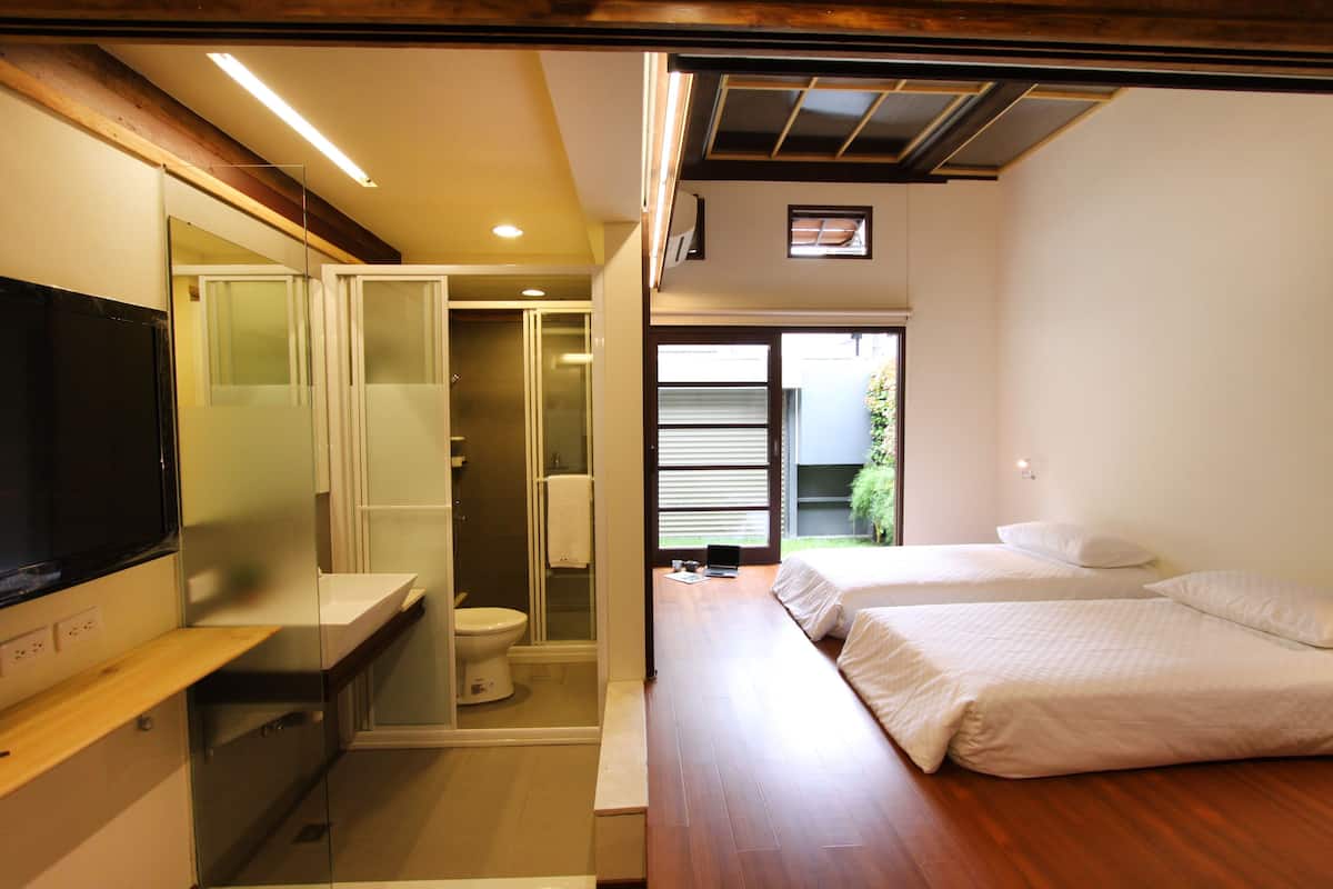 A modern hotel room with a wooden floor, a large bed, a TV, a bathroom with a toilet and shower, and a view of the outdoors.