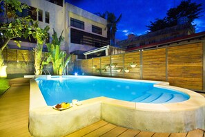 A swimming pool with a wooden deck, surrounded by a wooden fence, and potted plants.