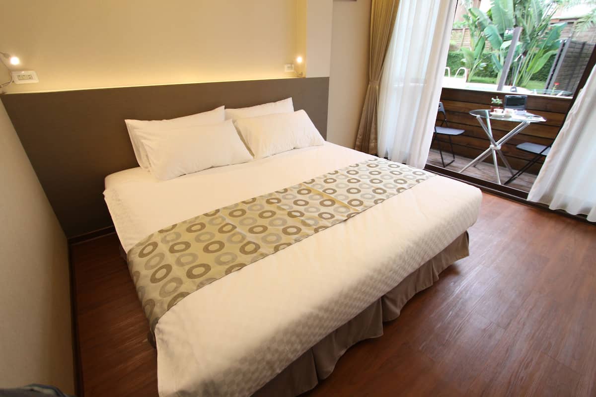 A neatly made bed with a patterned bedspread, a headboard, and a small table with chairs by a window.