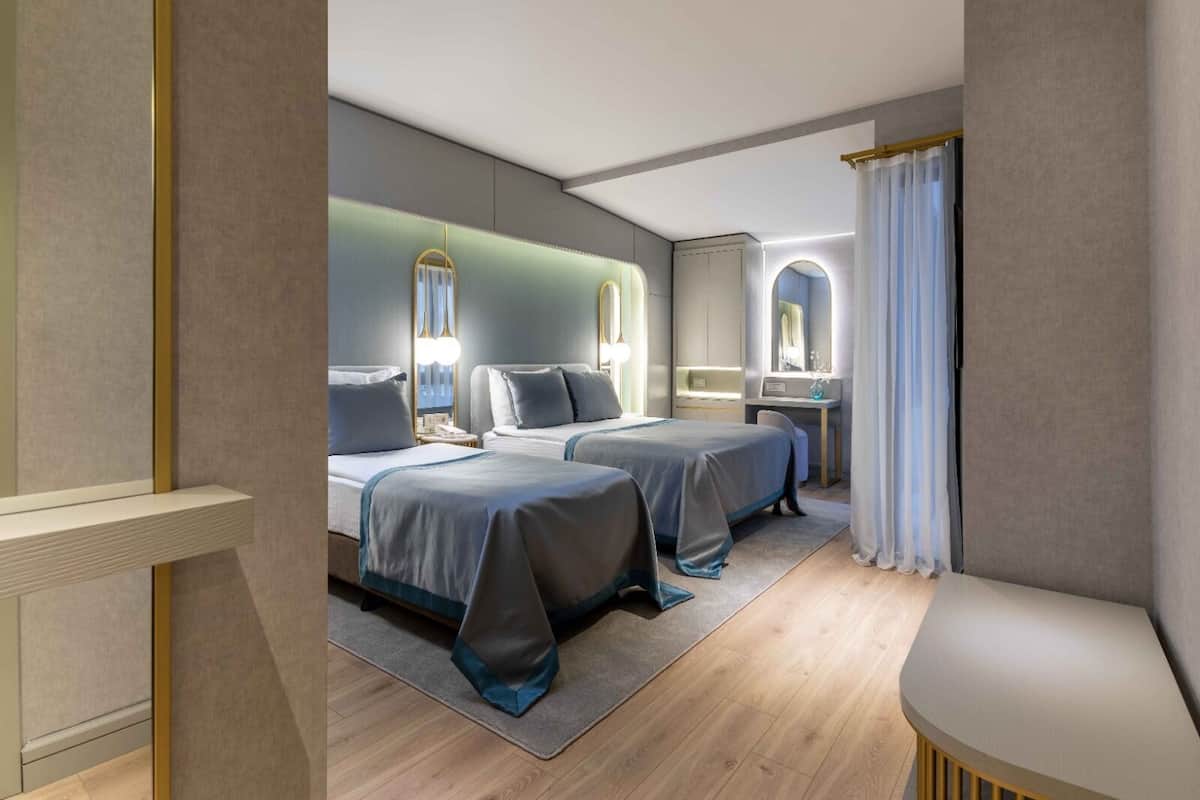 Une chambre d’hôtel avec deux lits, un bureau et une coiffeuse avec un miroir.
