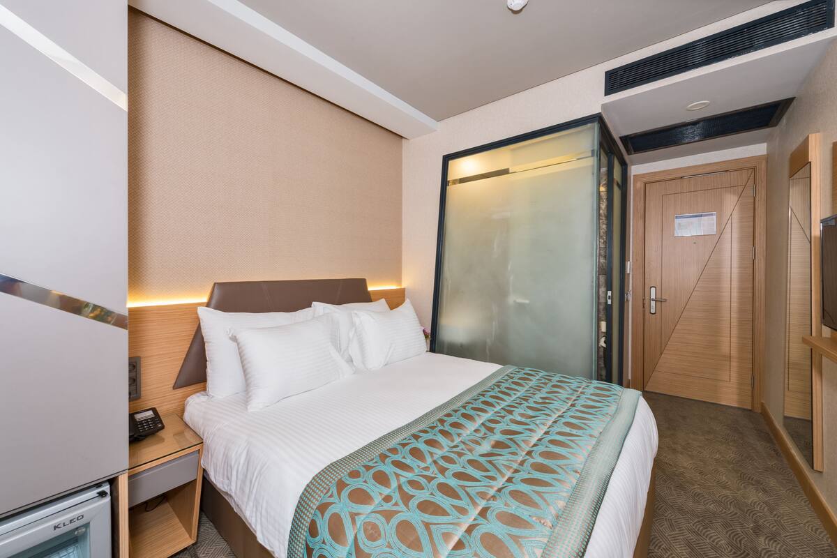 Une chambre d’hôtel comprenant un lit, une table de chevet avec un téléphone, un minibar, une armoire et un téléviseur.