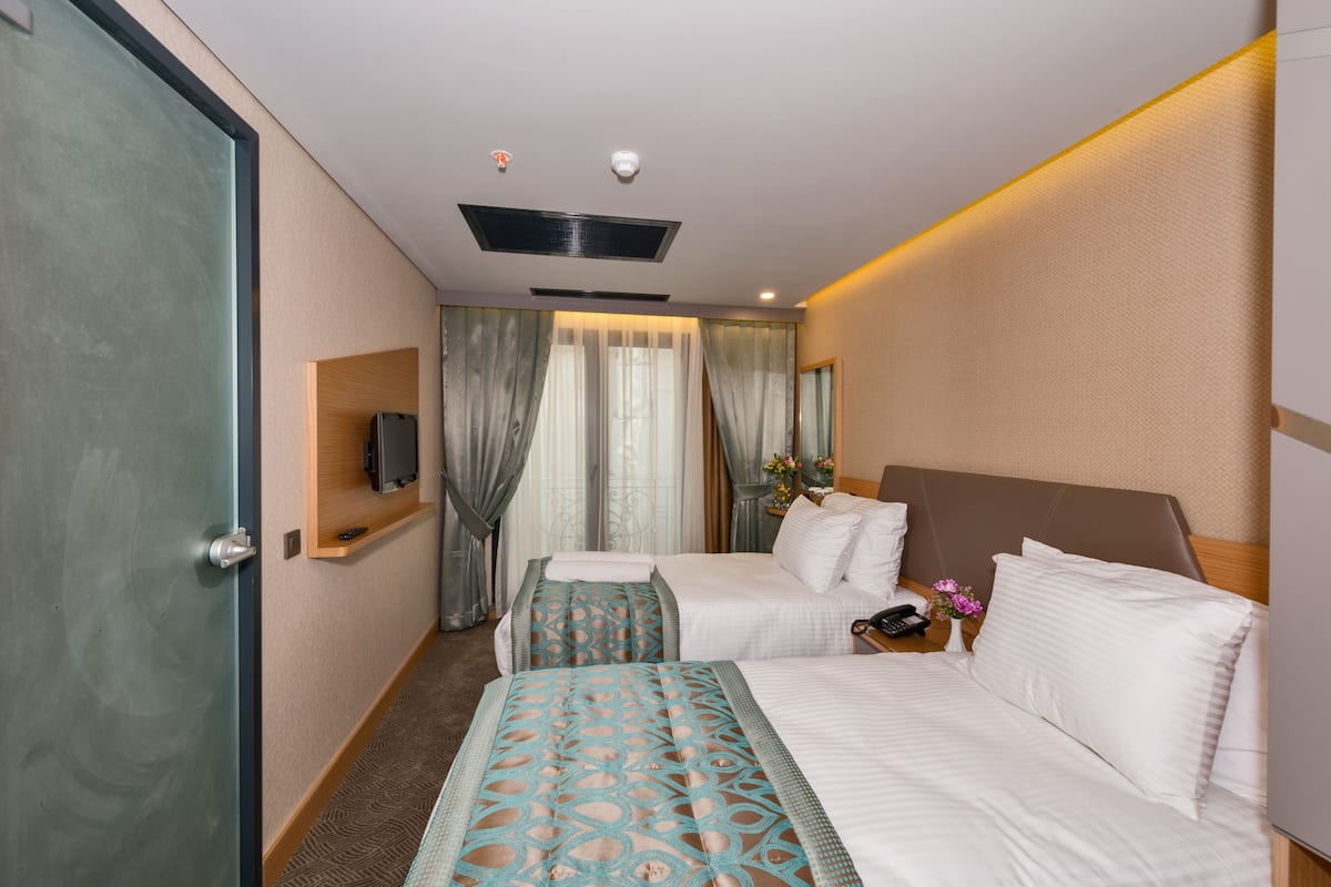 Une chambre d’hôtel avec deux lits, une télévision, une petite table avec un téléphone et un vase de fleurs, et une fenêtre avec des rideaux.