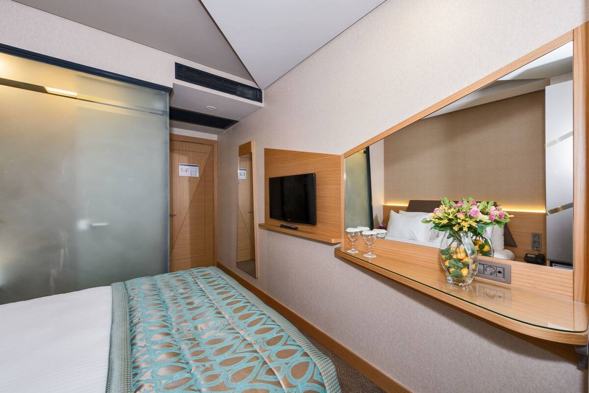 Une chambre d’hôtel comprenant un lit, une télévision, un miroir, une table de chevet avec un vase et une armoire.