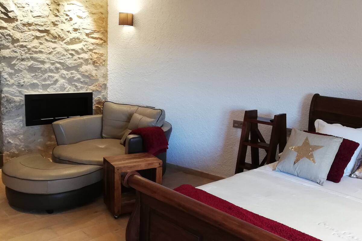 Quarto de hotel com parede de destaque em pedra, televisão, sofá, estrutura de cama de madeira e almofadas decorativas.