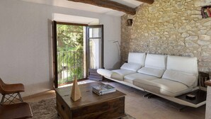 Un salon avec un mur en pierre, un canapé blanc, une table basse en bois et une vue sur l’extérieur, visible à travers une porte vitrée.