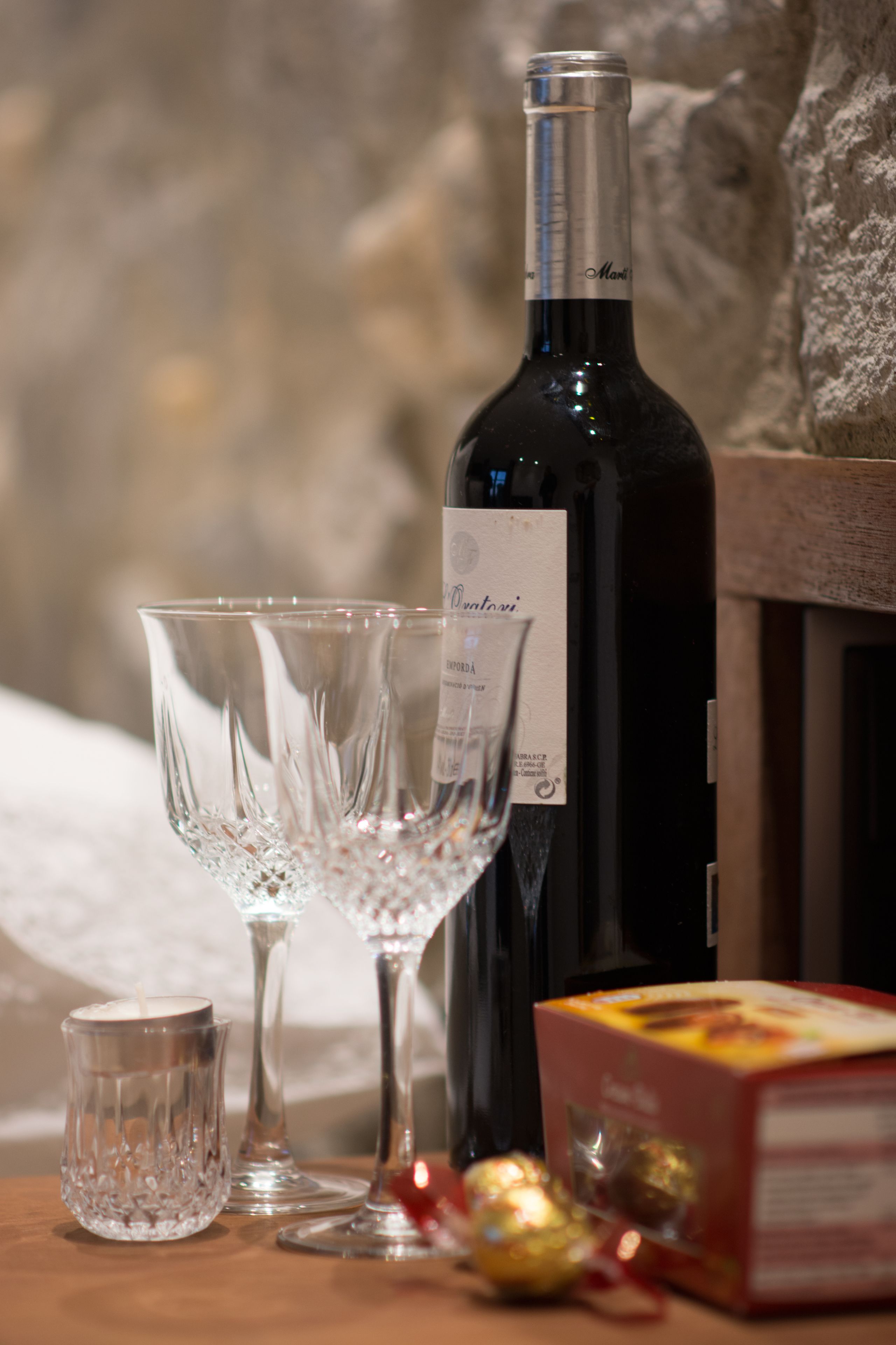 A bottle of wine, two wine glasses, a candle, and a box of chocolates on a wooden surface.