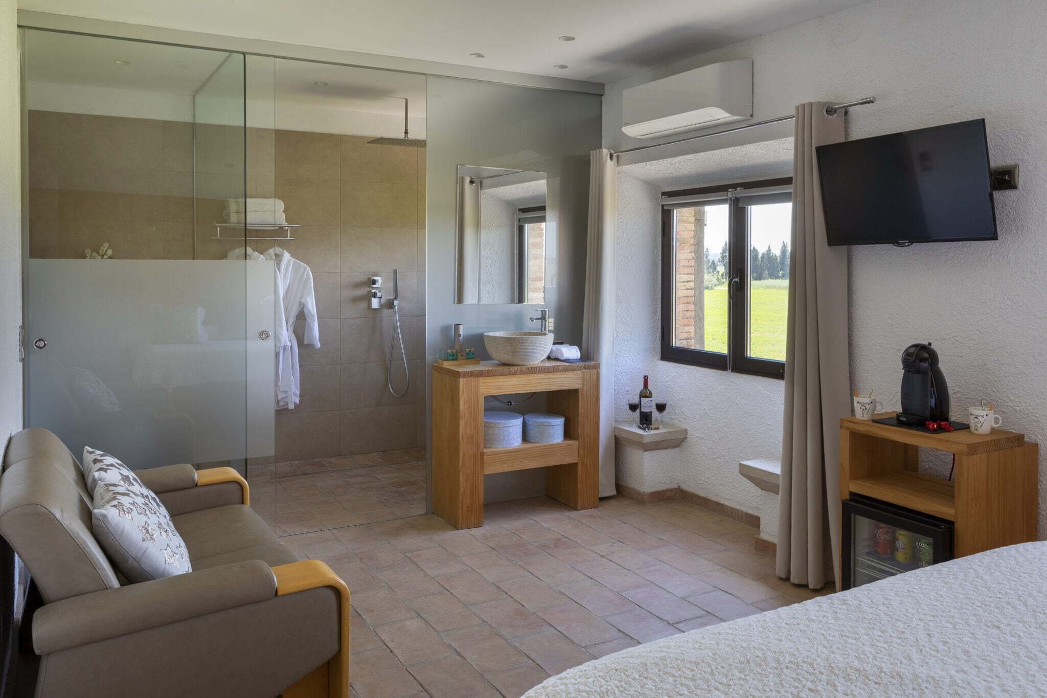 A modern bathroom with a glass shower enclosure, a wooden vanity, a sink, and a television mounted on the wall.