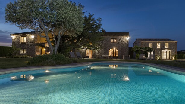 Une grande maison avec une piscine, des murs en pierre et un arbre devant.