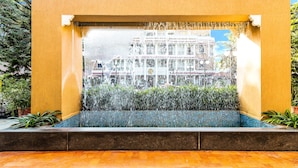 A fountain with water cascading into a tiled pool, surrounded by a yellow wall and greenery. - FabHotel Rajwada Baner (Pune)