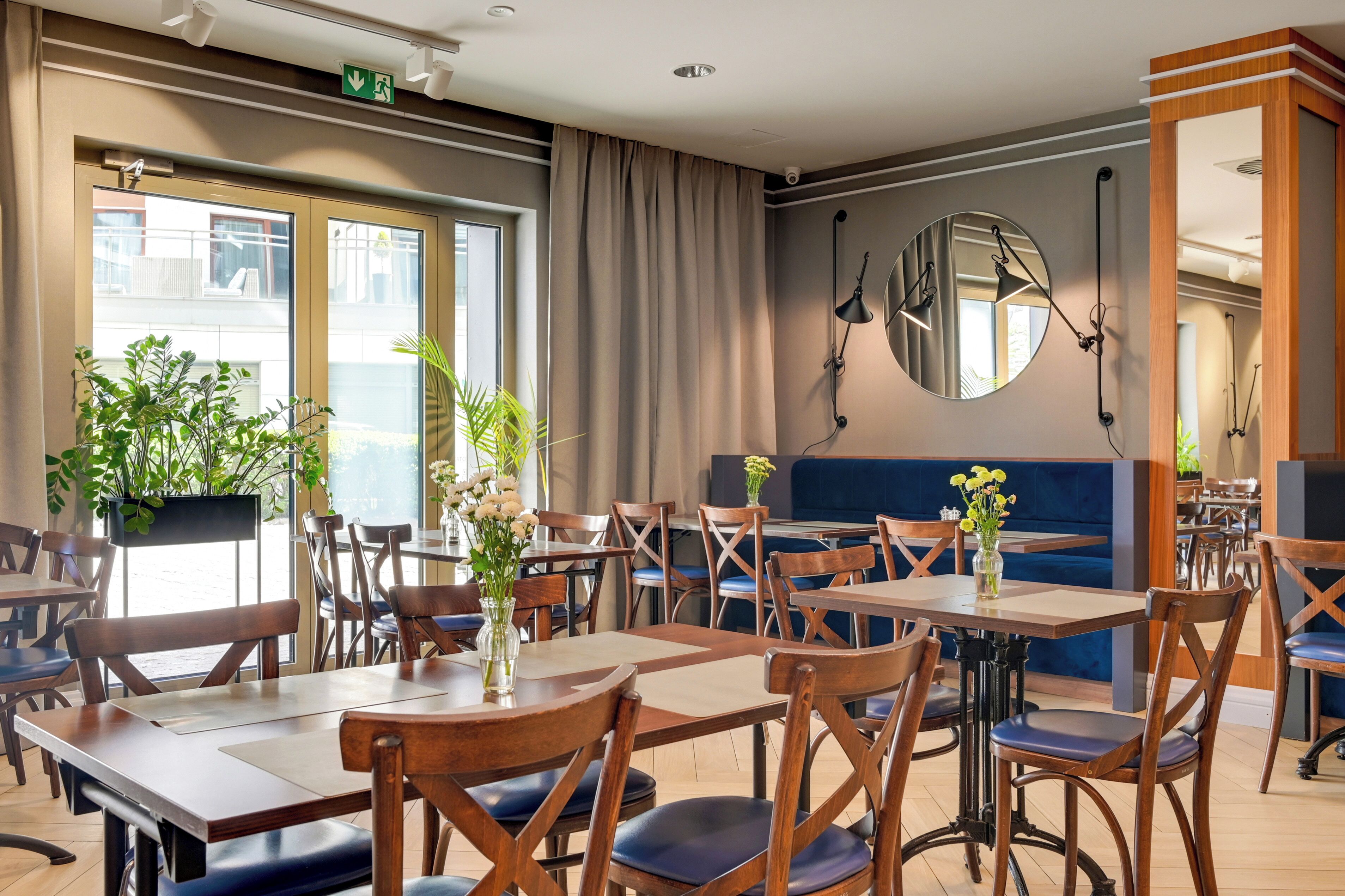 A restaurant with wooden tables and chairs, potted plants, and a large mirror on the wall.