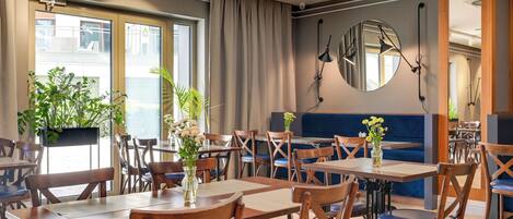 A restaurant with wooden tables and chairs, potted plants, and a large mirror on the wall.