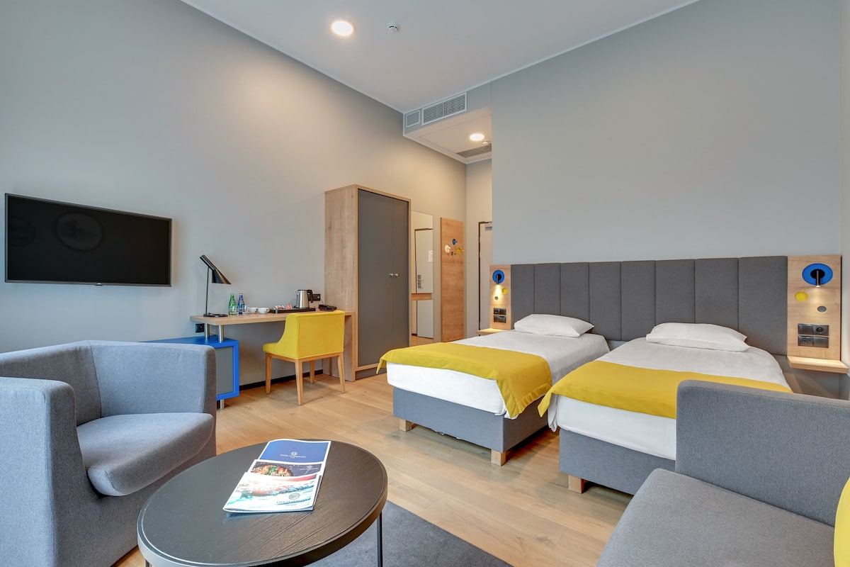 A modern hotel room with two beds, a desk, a chair, and a small table.