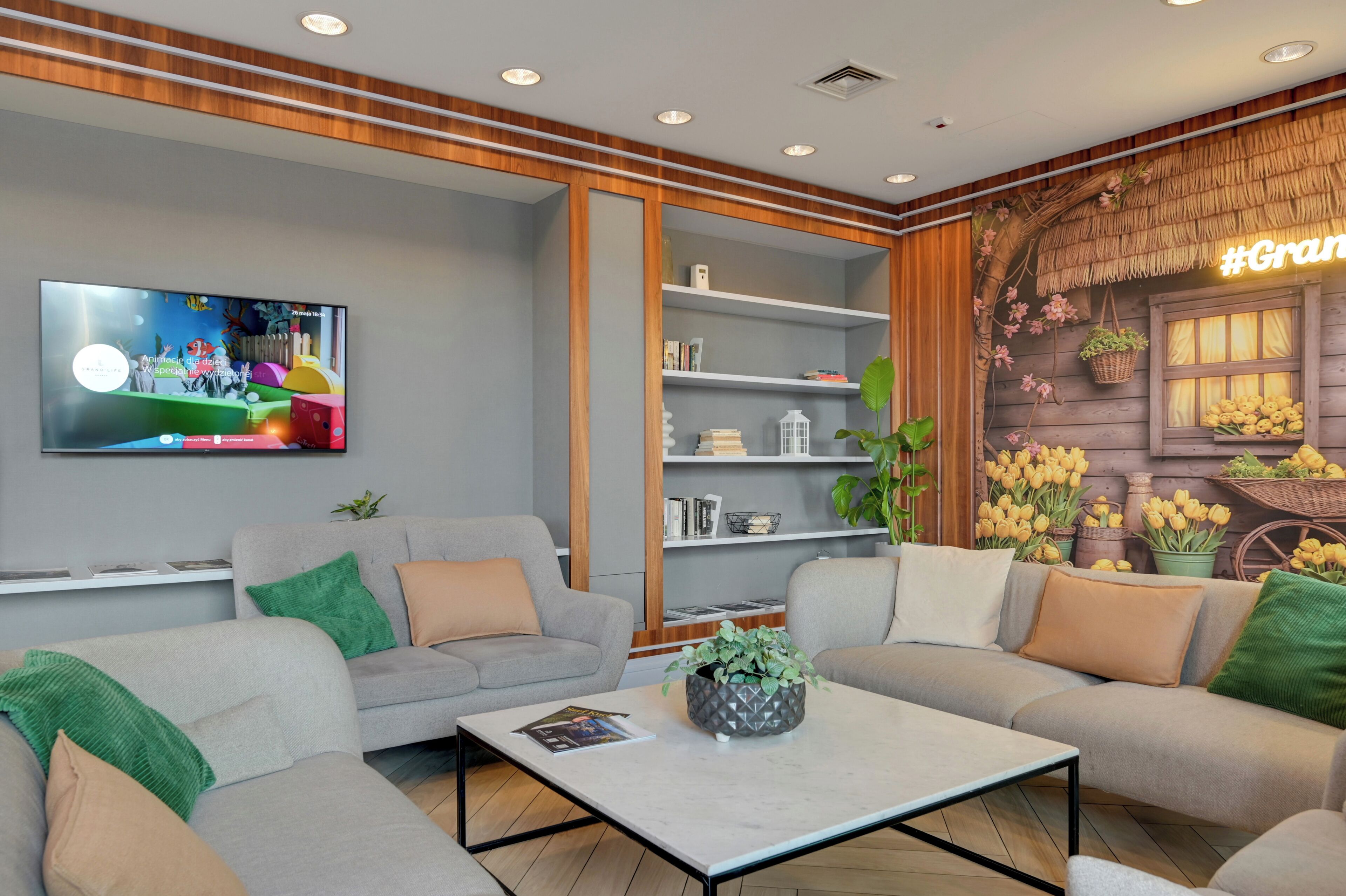 A modern living room with grey sofas, a coffee table, and a TV mounted on the wall.