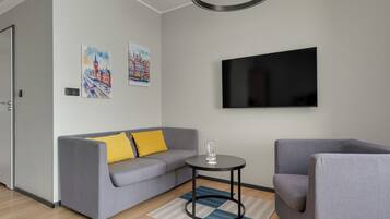 A modern living room with a grey sofa, a small round table, a flat-screen TV, and two paintings on the wall.
