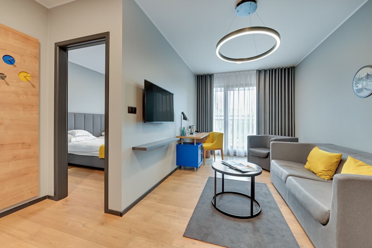 A modern hotel room with a bed, a sofa, a desk, and a TV.