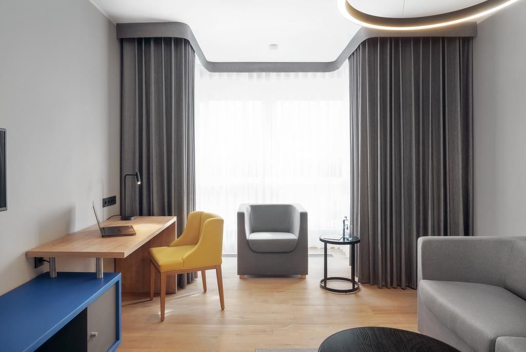 Un salon moderne avec un bureau en bois, une chaise jaune, un canapé gris et un fauteuil gris.