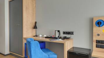 Una habitación pequeña con escritorio, una silla, kitchenette y armario.
